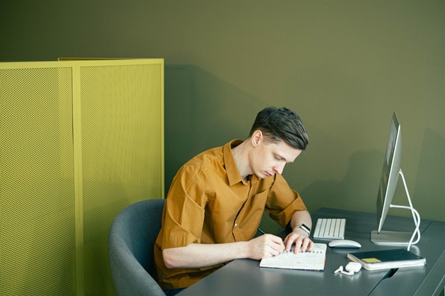 a man noting down ideas in front of a computer