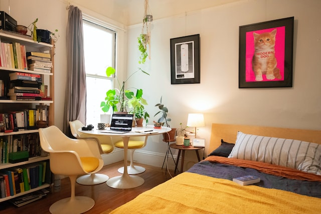 A bedroom with office space in the corner decorated with house plants and a bookshelf.
