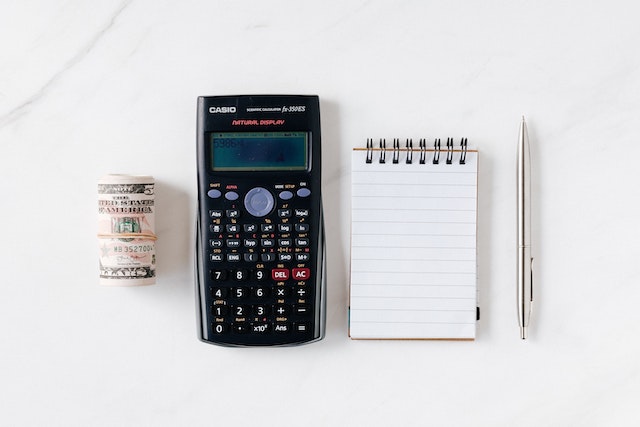 A notepad, a pen, a calculator, and some cash