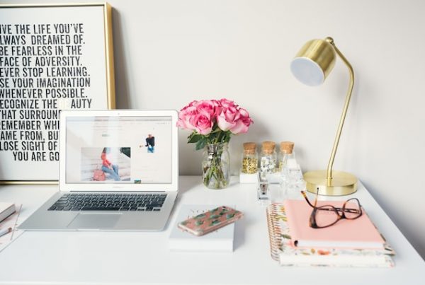 Home office desk with a pink notepad, a bouquet of roses, a laptop, framed motivational poster in a home that fosters creativity.
