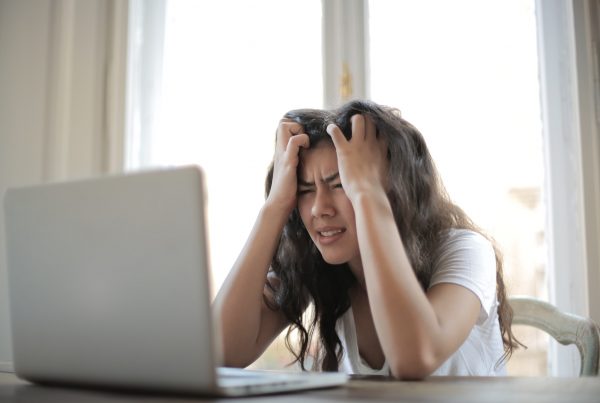 A woman at her laptop, gripping her head in distress while looking for effective strategies for tackling freelancer burnout